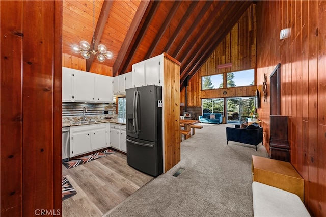 kitchen featuring wood walls, a sink, high vaulted ceiling, a notable chandelier, and black fridge
