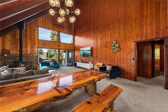 carpeted living room featuring a wood stove, a chandelier, wooden walls, and high vaulted ceiling
