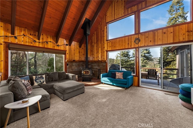 carpeted living room featuring high vaulted ceiling, wood walls, a wood stove, wood ceiling, and beam ceiling