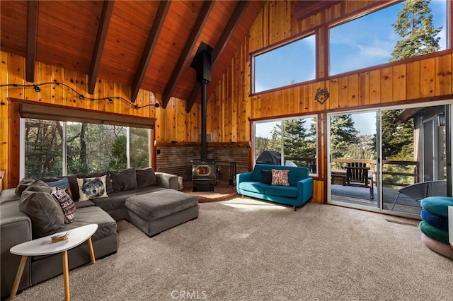 living room featuring wooden walls, carpet, beamed ceiling, wooden ceiling, and a wood stove