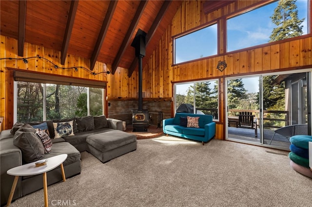 carpeted living area featuring wooden walls, beam ceiling, a wood stove, high vaulted ceiling, and wood ceiling