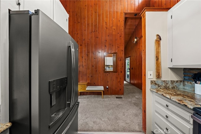 kitchen with white cabinetry, stainless steel fridge, wooden walls, carpet flooring, and light stone countertops