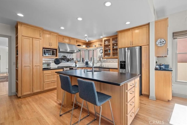 kitchen with sink, a breakfast bar area, appliances with stainless steel finishes, a center island with sink, and light wood-type flooring