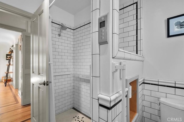 bathroom featuring hardwood / wood-style floors, tiled shower, tile walls, and toilet