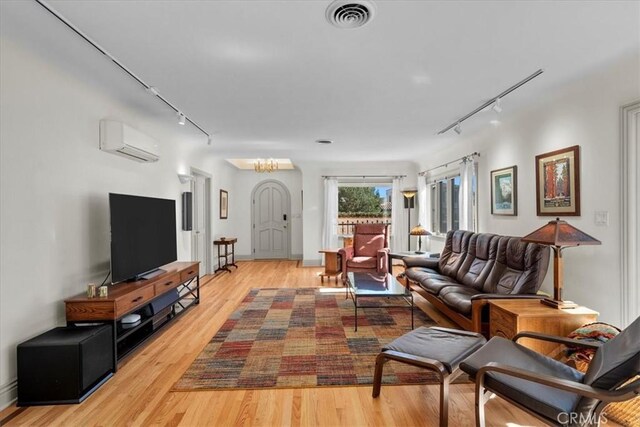 living room featuring an AC wall unit, a chandelier, track lighting, and light wood-type flooring