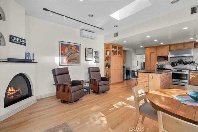 interior space featuring a kitchen island, appliances with stainless steel finishes, a wall mounted air conditioner, a skylight, and light wood-type flooring