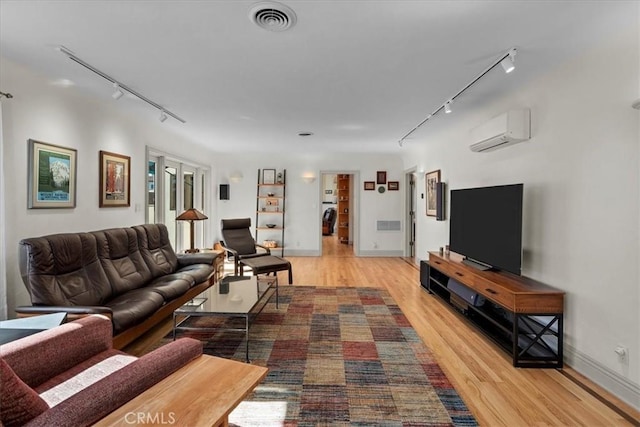 living room featuring a wall mounted air conditioner, track lighting, and light hardwood / wood-style floors