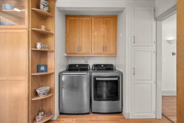 clothes washing area with cabinets, light hardwood / wood-style floors, and washer and dryer