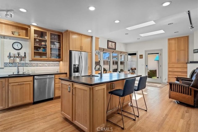 kitchen featuring sink, stainless steel appliances, an island with sink, and light wood-type flooring