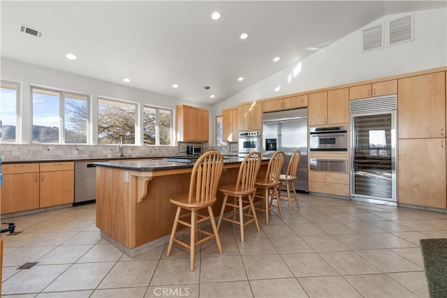 kitchen featuring stainless steel appliances, light tile patterned flooring, a kitchen island, and decorative backsplash