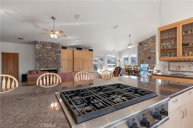 kitchen featuring a stone fireplace, sink, vaulted ceiling, dark stone countertops, and ceiling fan