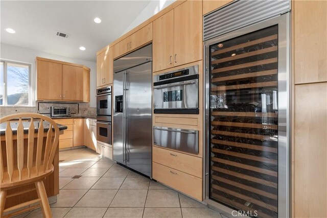 kitchen with light brown cabinetry, lofted ceiling, wine cooler, light tile patterned floors, and stainless steel appliances