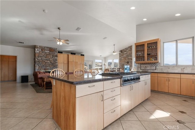 kitchen featuring light tile patterned flooring, a center island, vaulted ceiling, dark stone countertops, and stainless steel gas stovetop