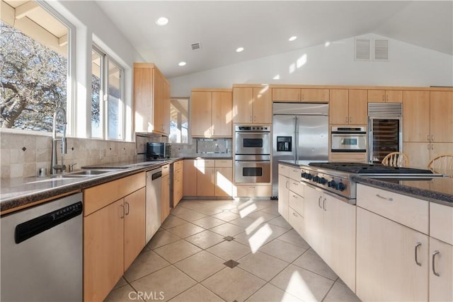 kitchen featuring light brown cabinetry, vaulted ceiling, light tile patterned floors, stainless steel appliances, and decorative backsplash