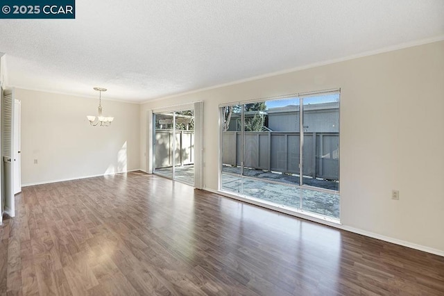 empty room with hardwood / wood-style floors, a textured ceiling, ornamental molding, and a chandelier