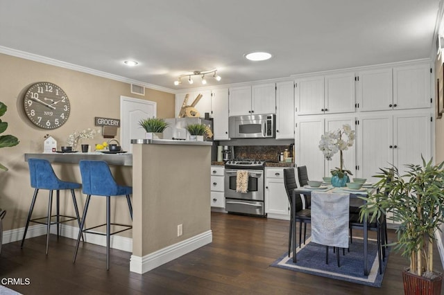 kitchen featuring white cabinetry, dark hardwood / wood-style flooring, stainless steel appliances, and a kitchen breakfast bar