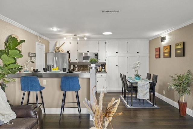 kitchen featuring appliances with stainless steel finishes, a breakfast bar, white cabinets, ornamental molding, and dark wood-type flooring