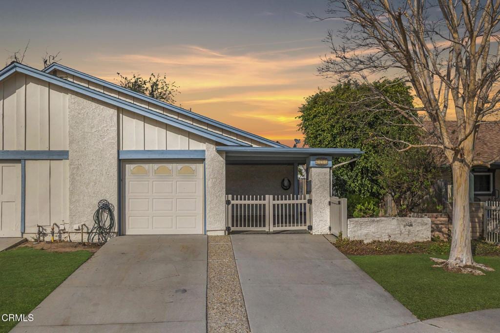 mid-century modern home with fence, an attached garage, stucco siding, concrete driveway, and board and batten siding