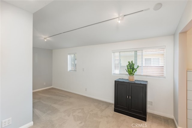 carpeted empty room featuring lofted ceiling and track lighting