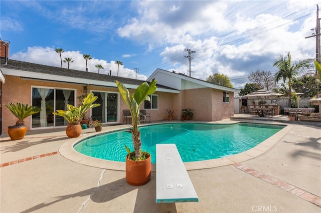 view of swimming pool featuring a patio and a diving board