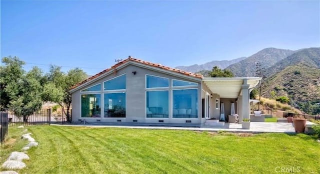 back of property featuring a mountain view, a patio area, and a lawn