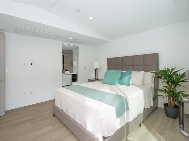 bedroom with vaulted ceiling, connected bathroom, and light hardwood / wood-style floors