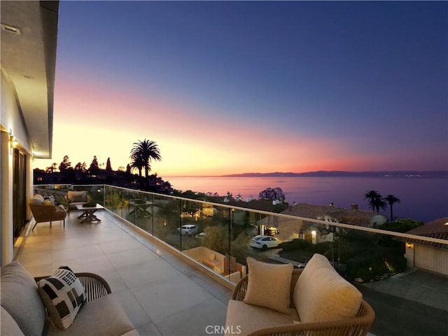 balcony at dusk featuring a water view and outdoor lounge area