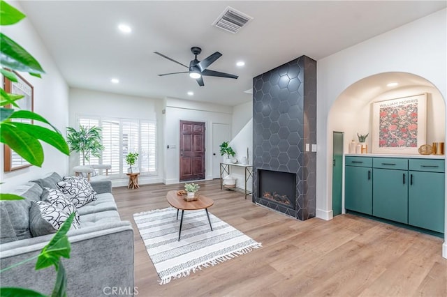 living room featuring ceiling fan, a large fireplace, and light wood-type flooring