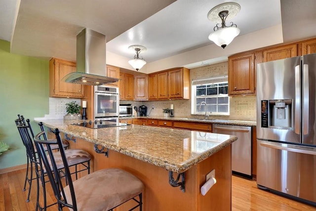 kitchen featuring hanging light fixtures, a kitchen breakfast bar, island exhaust hood, stainless steel appliances, and light stone countertops