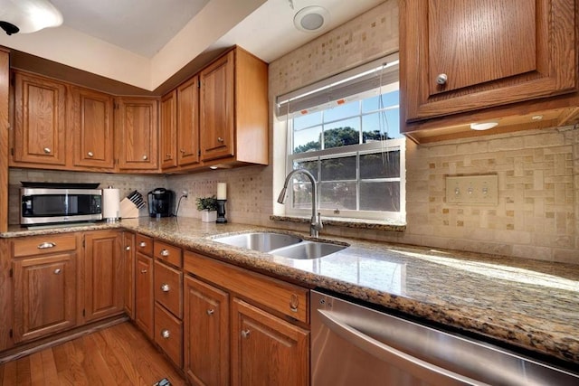 kitchen with appliances with stainless steel finishes, tasteful backsplash, sink, light stone counters, and light wood-type flooring