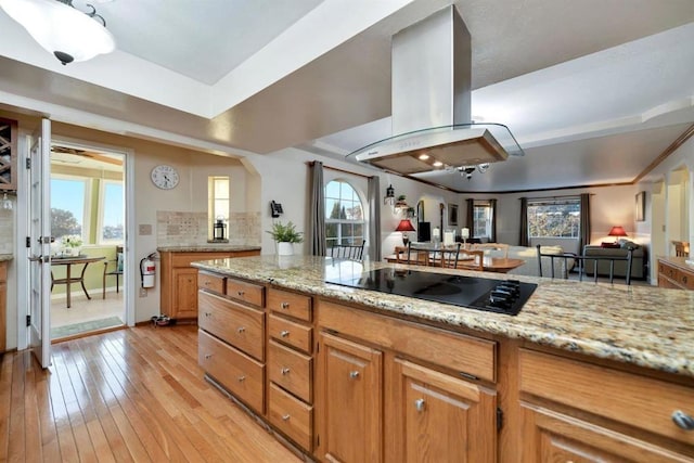 kitchen featuring light stone counters, island range hood, light hardwood / wood-style floors, a healthy amount of sunlight, and black electric cooktop