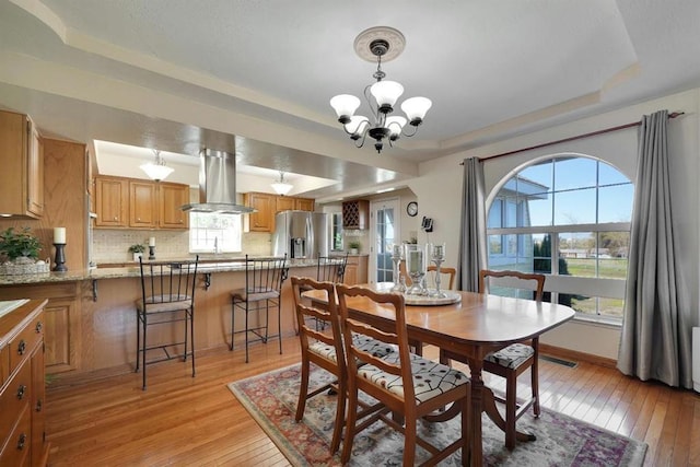 dining room with an inviting chandelier, a tray ceiling, and light wood-type flooring