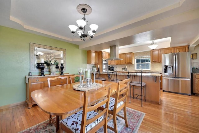 dining space with a tray ceiling, light hardwood / wood-style floors, and a chandelier