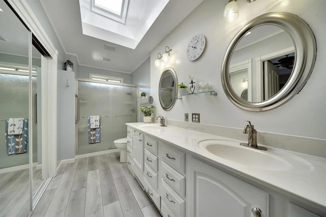 bathroom featuring a skylight, vanity, wood-type flooring, a shower with shower door, and toilet