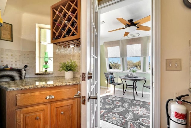 bar featuring light stone counters, decorative backsplash, ceiling fan, and light tile patterned flooring