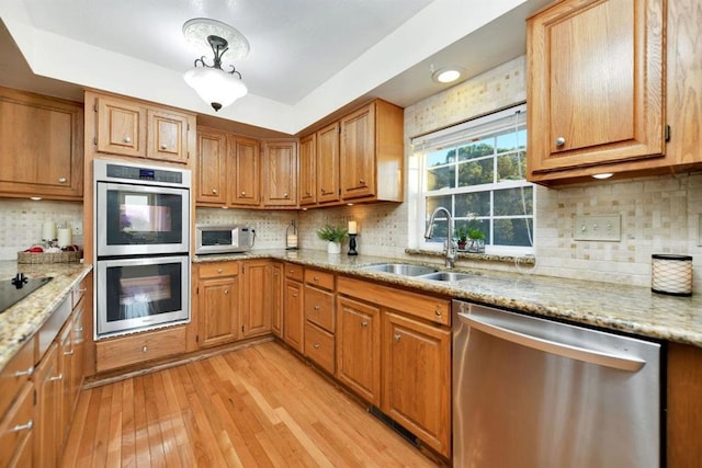 kitchen featuring sink, appliances with stainless steel finishes, tasteful backsplash, light stone countertops, and light wood-type flooring