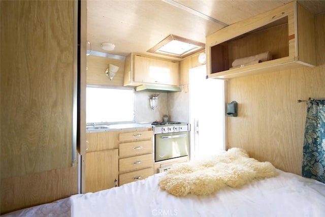 kitchen with stainless steel range with gas cooktop, light brown cabinetry, and a skylight