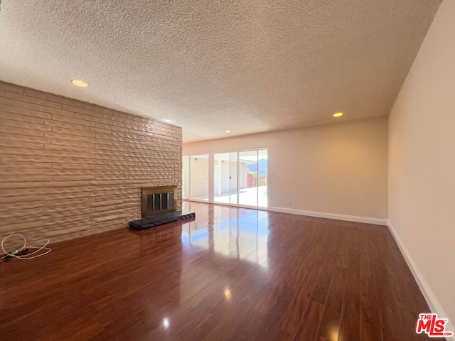 unfurnished living room with dark hardwood / wood-style flooring, a brick fireplace, and a textured ceiling