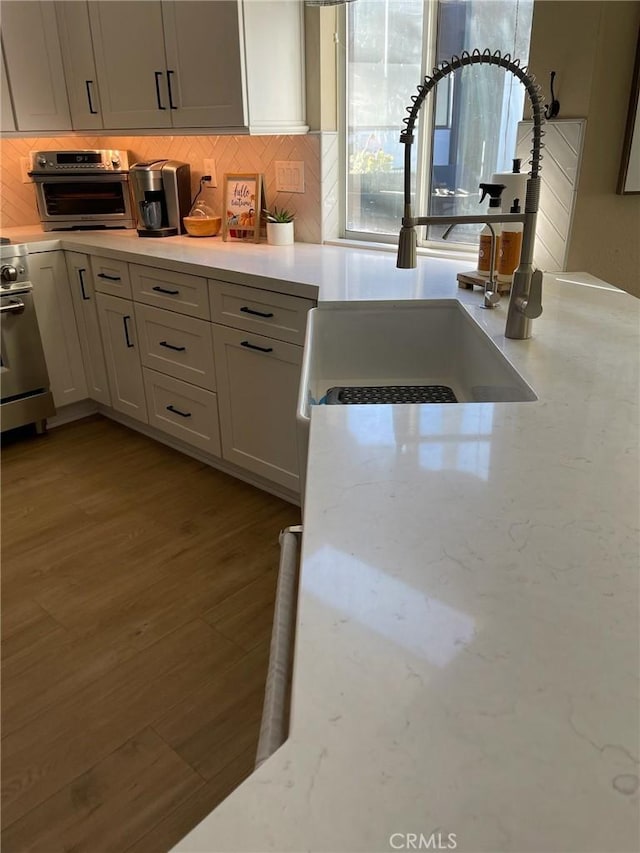 kitchen with sink, light hardwood / wood-style flooring, tasteful backsplash, light stone countertops, and white cabinets