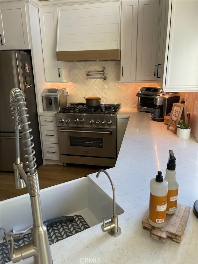 kitchen with tasteful backsplash, white cabinetry, stainless steel appliances, light stone countertops, and wall chimney range hood