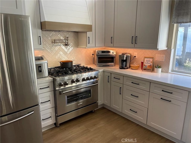 kitchen featuring tasteful backsplash, appliances with stainless steel finishes, custom range hood, and light hardwood / wood-style flooring