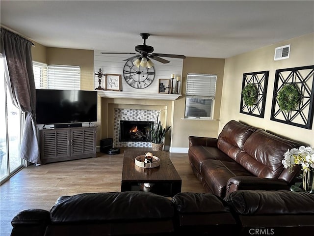 living room featuring light hardwood / wood-style flooring, a tile fireplace, and ceiling fan