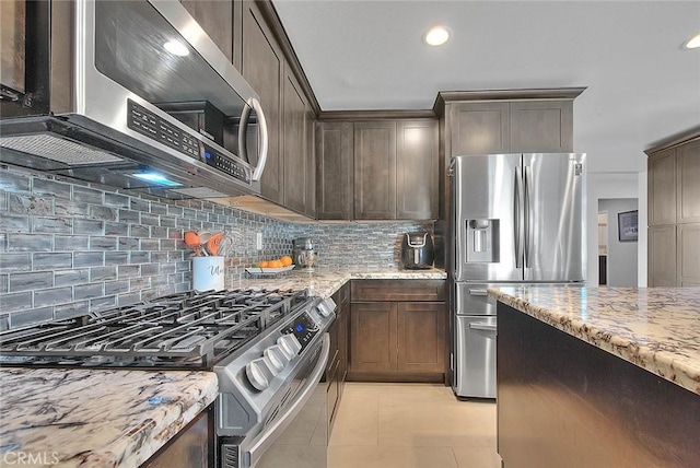 kitchen featuring dark brown cabinetry, light tile patterned floors, stainless steel appliances, light stone countertops, and decorative backsplash