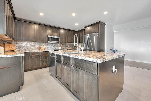 kitchen featuring dark brown cabinetry, appliances with stainless steel finishes, a center island with sink, and backsplash