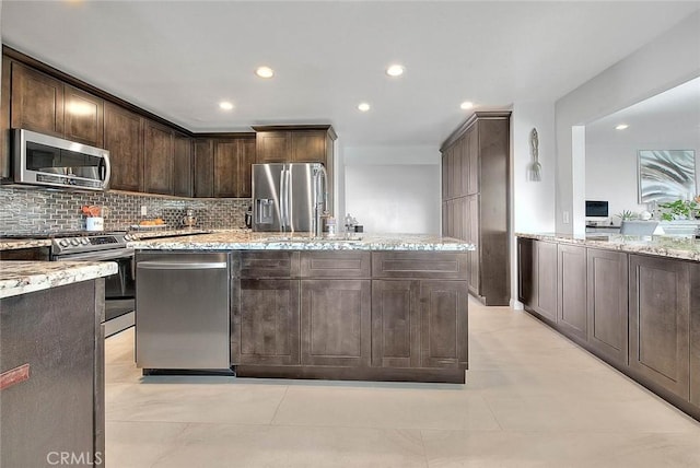 kitchen featuring a kitchen island, tasteful backsplash, light stone counters, dark brown cabinetry, and stainless steel appliances