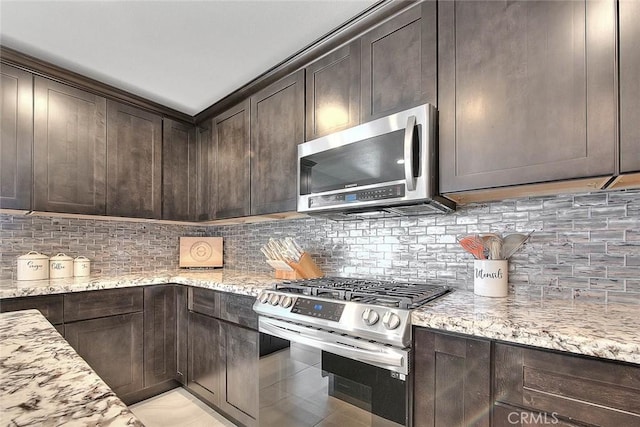 kitchen featuring backsplash, dark brown cabinets, light stone countertops, and appliances with stainless steel finishes