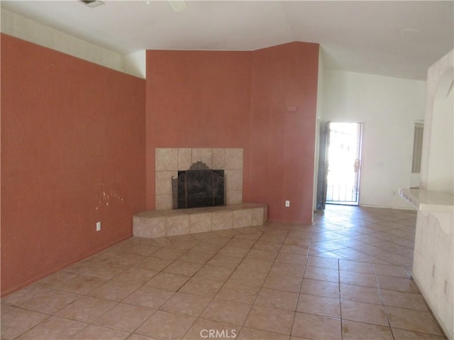 unfurnished living room with a tiled fireplace, lofted ceiling, and light tile patterned flooring