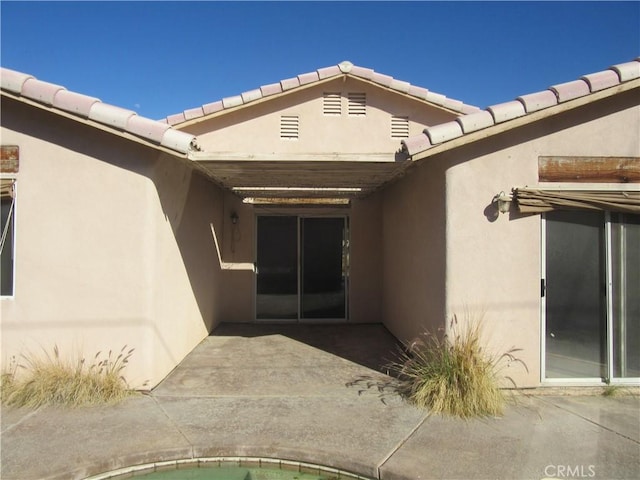 view of exterior entry featuring a tiled roof, a patio area, and stucco siding