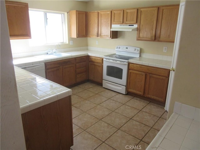 kitchen featuring white appliances, tile counters, under cabinet range hood, and a sink