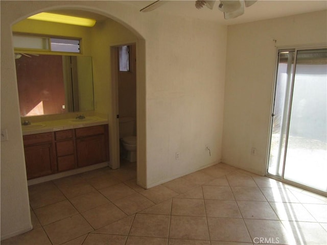 interior space featuring arched walkways, light tile patterned floors, a ceiling fan, and a sink